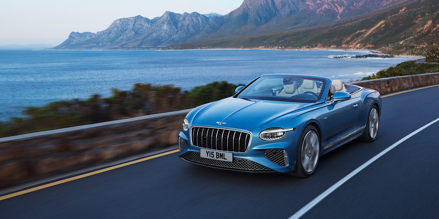 Bentley Zug New Bentley Continental GTC Azure convertible in Light Windsor blue paint with 22 inch Azure wheels and chrome grill, driving dynamically by the sea