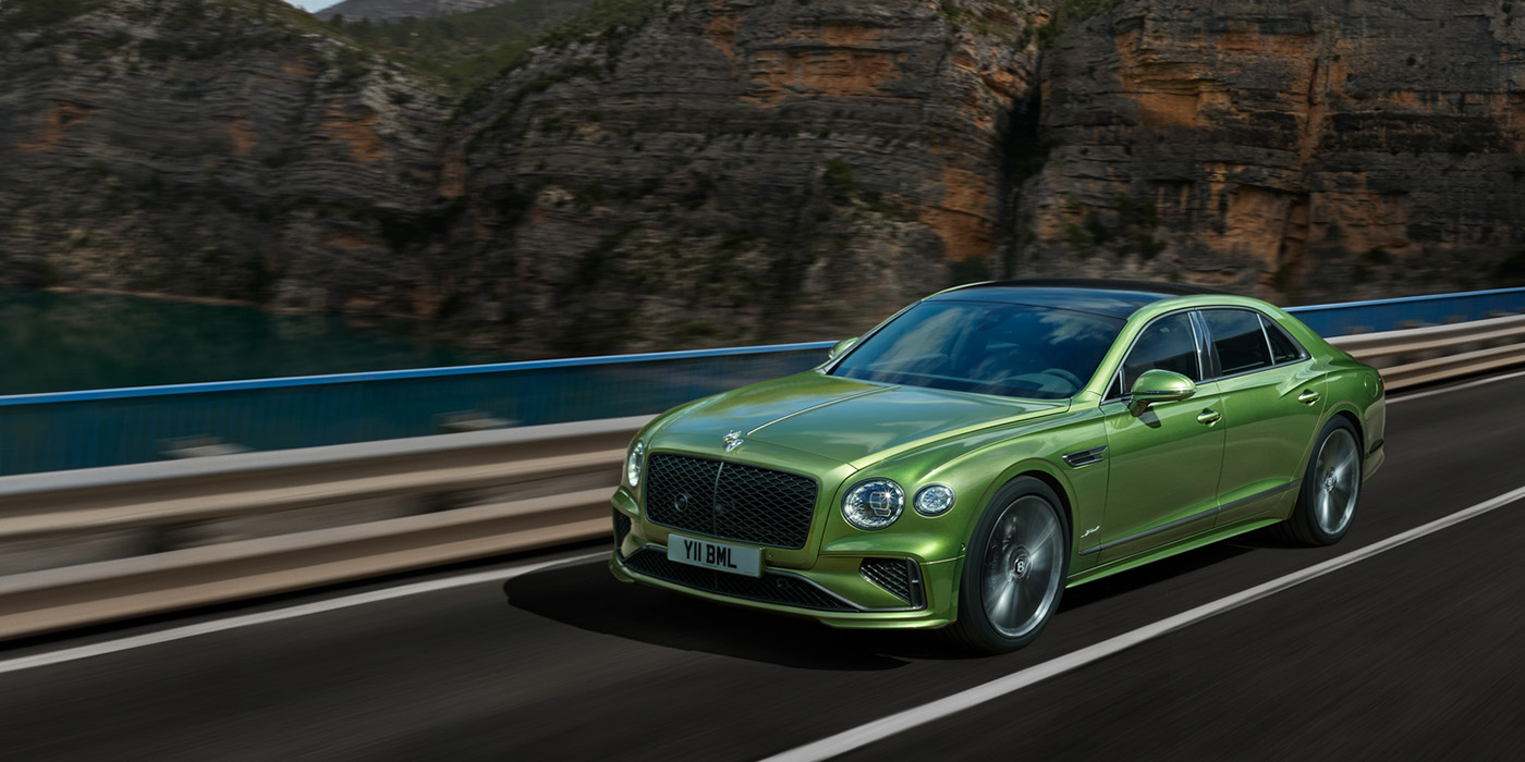 Bentley Zug Bentley New Flying Spur Speed v8 hybrid sedan driving dynamically on a mountain road in Tourmaline Green paint