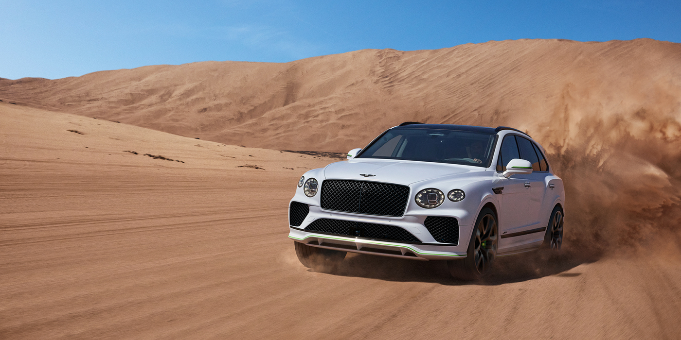 Bentley Zug Bentley Bentayga Speed SUV front three quarter in Snow Quarts Pearlescent by Mulliner white paint driving dynamically through the desert