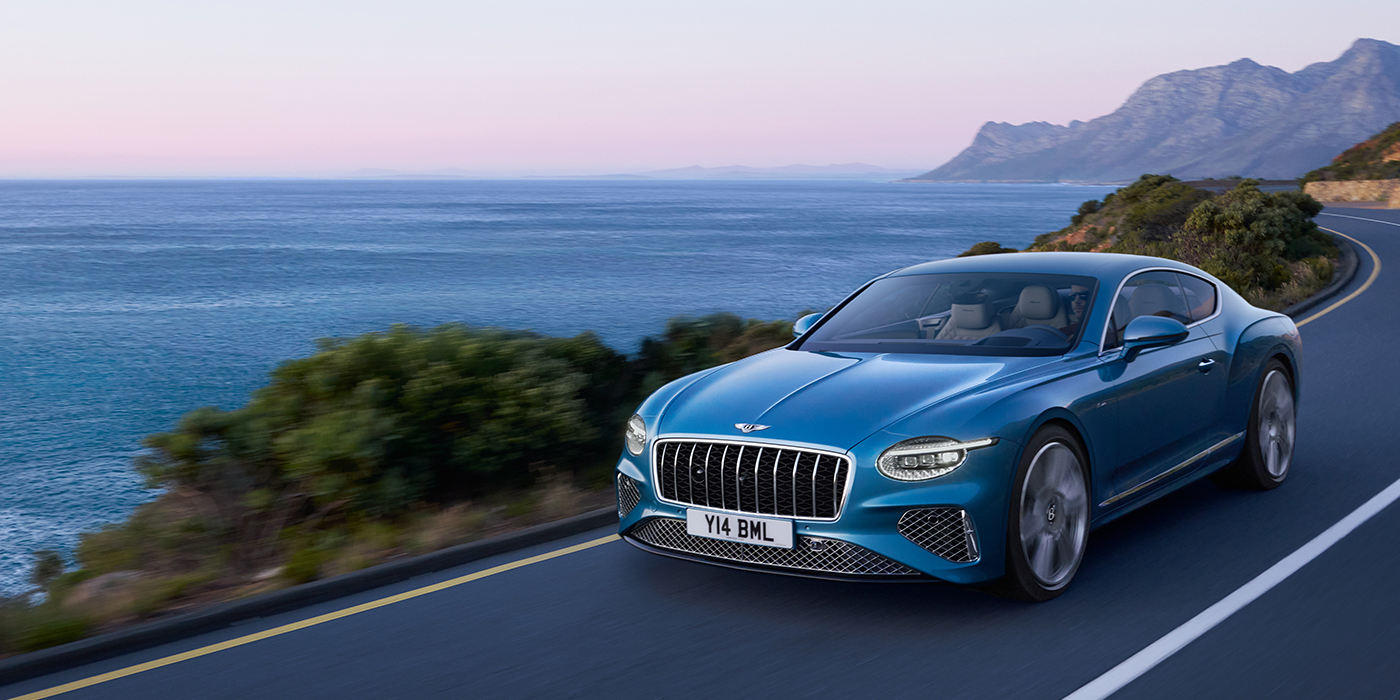 Bentley Zug New Bentley Continental GT Azure coupe in Light Windsor blue paint with 22 inch Azure wheels and chrome grill, driving dynamically by the sea