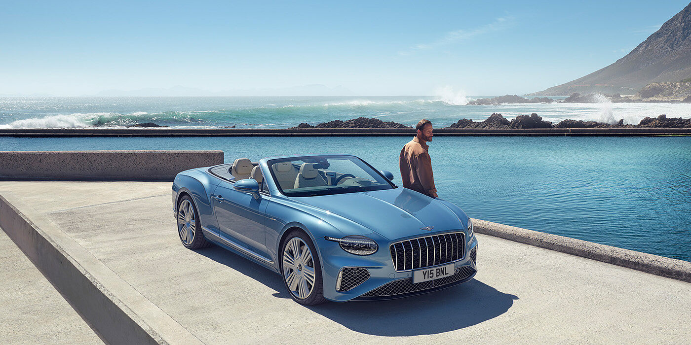 Bentley Zug New Bentley Continental GTC Azure convertible front view in Light Windsor blue paint with 22 inch ten spoke wheels parked by the sea in the sunshine