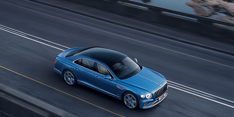 Bentley Zug New Bentley Flying Spur Azure sedan in Light windsor blue paint by Mulliner, with 22 inch Azure wheels seen from overhead driving dynamically on a country road