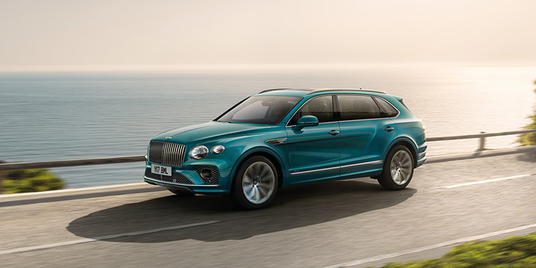 Bentley Zug Bentley Bentayga Extended Wheelbase Azure SUV in Topaz blue paint driving dynamically by the ocean