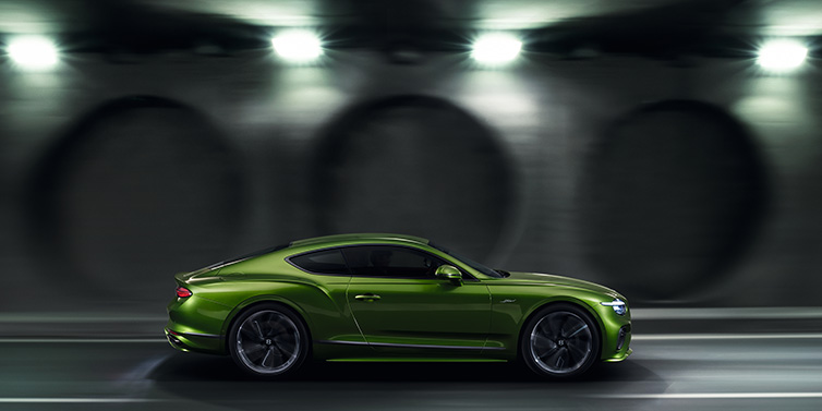 Bentley Zug Bentley Continental GT Speed coupe profile in Tourmaline Green driving dynamically past a concrete wall at night