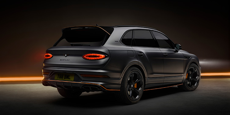 Bentley Zug Bentley Bentayga S Black Edition SUV rear three quarter in Anthracite Satin paint against a dark red and yellow background