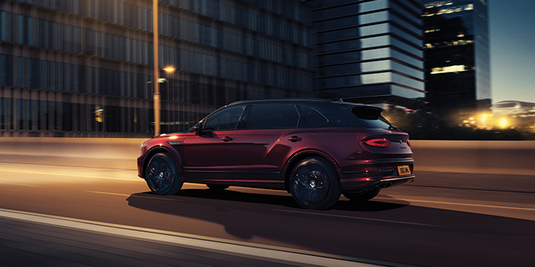 Bentley Zug Bentley Bentayga Extended Wheelbase Mulliner SUV in Cricket Ball red paint driving dynamically in city at night