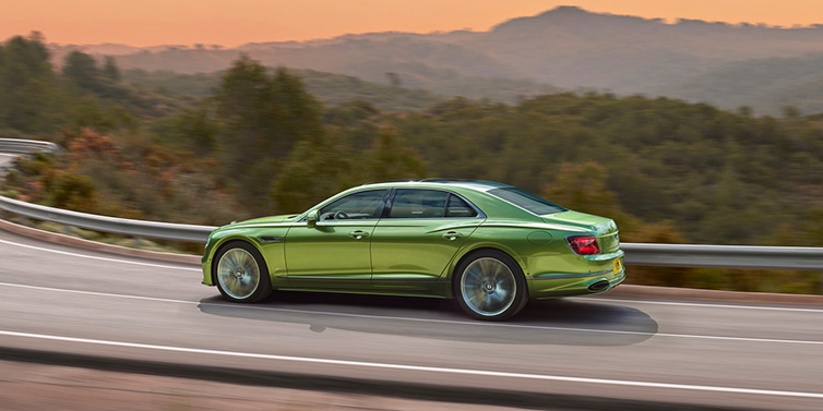 Bentley Zug Bentley Flying Spur Speed sedan side profile in Tourmaline Green paint driving dynamically on a mountain road at sunset