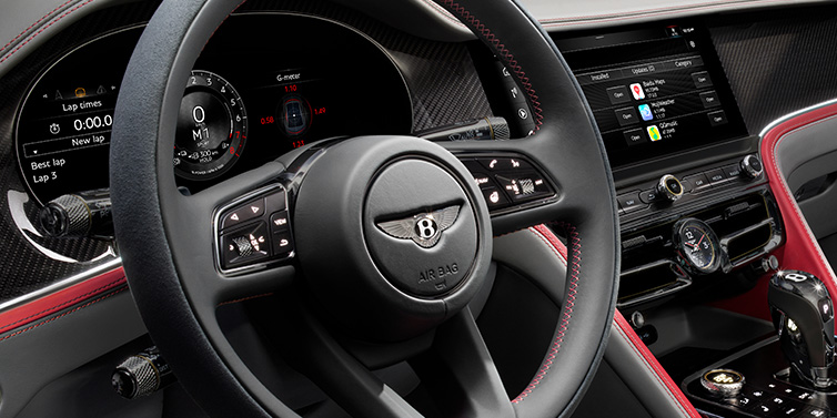 Bentley Zug Bentley Flying Spur Speed sedan front interior detail showing steering wheel and driver screens surrounded with Hotspur red and Gravity Grey hides